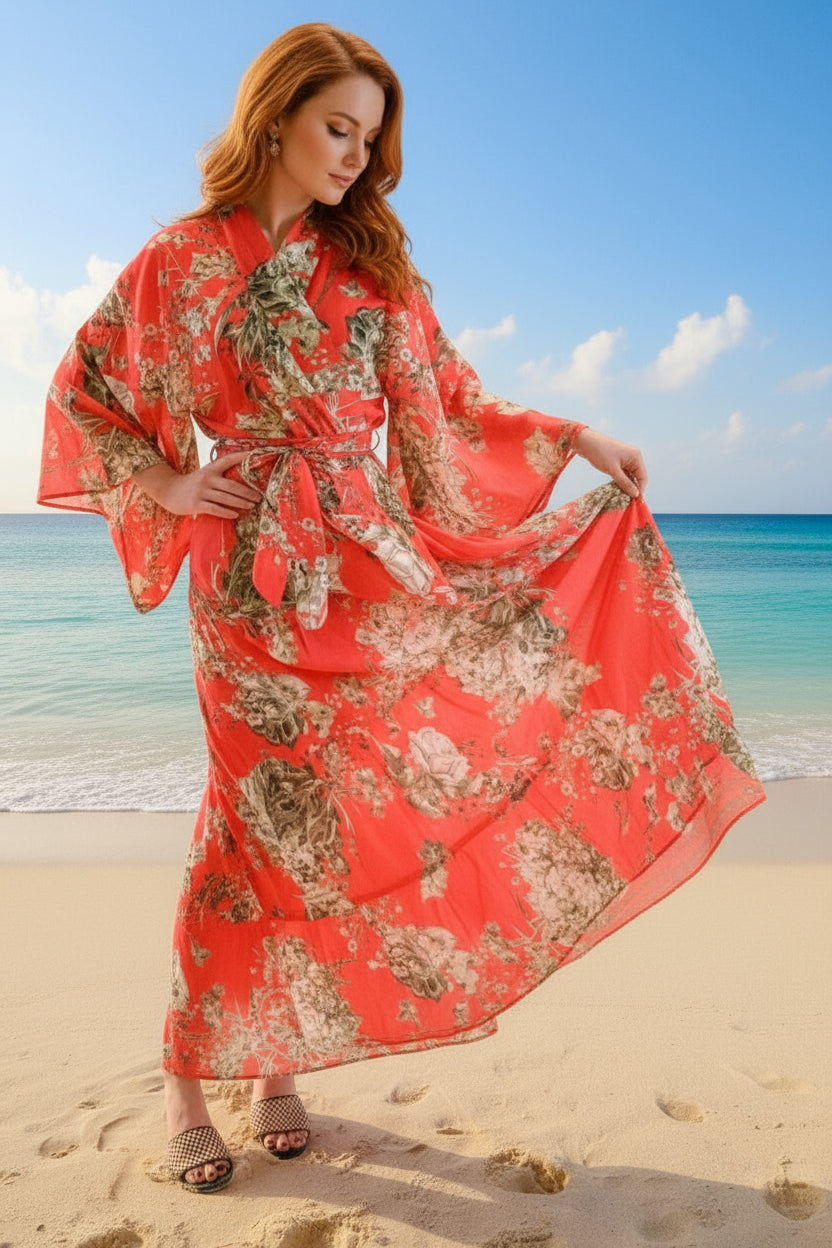 Woman in a red floral dress standing on a beach with blue sky and ocean.