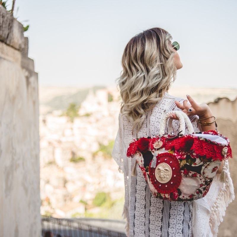 A girl with a Coffa on her shoulder in a sunny sicilian landscape