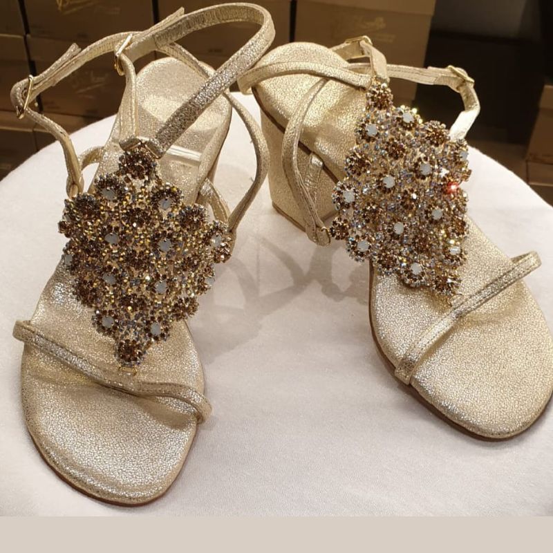 A pair of beige capri sandals with a decorative jewel on the toe and a wooden heel with a non-slip rubber pad.