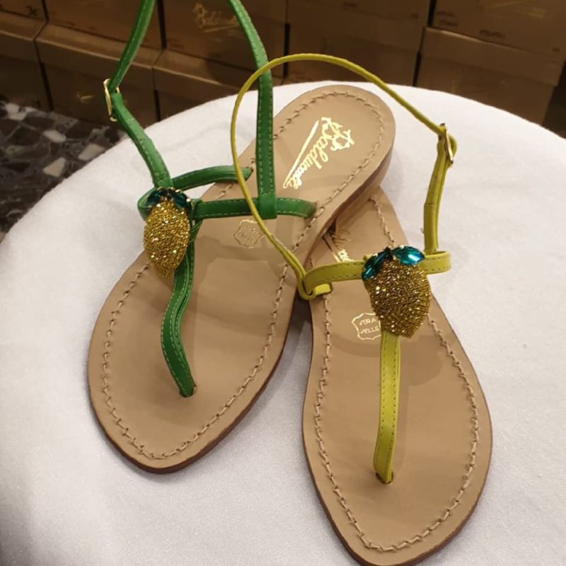 A pair of green leather sandals with yellow Swarovski jewels and blue soft plantar, hand stitched and displayed on a flat surface.