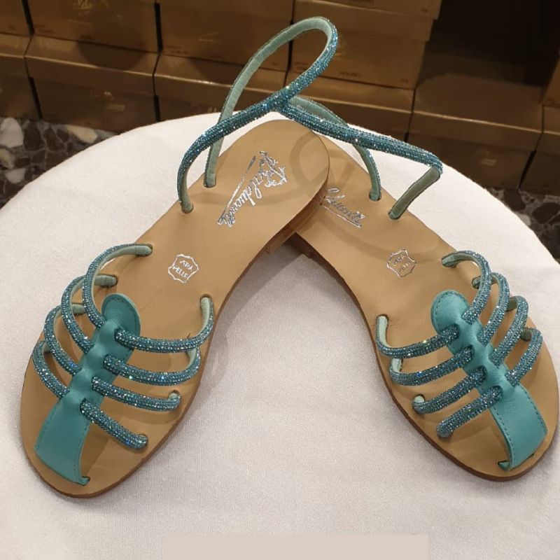 A pair of Ragno Bijoux Handmade Capri Sandals with green straps and a brown leather upper, displayed against a backdrop of boxes.