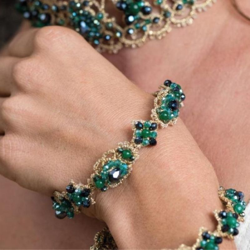 A hand wearing a green and blue beaded bracelet with gold detailing.